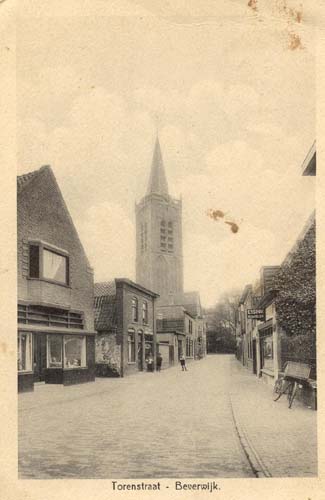 Torenstraat
Wij zijn in de kerkbuurt, het allereerste begin van Beverwijk, waar de eerste St. Agathakerk werd gebouwd (eigenlijk nog een kapel). De kapel werd gebouwd nadat het meisje Altruda als door een wonder gered werd uit de handen van boosdoener hertog Rorik, die beleend was met Kennemerland. Zij riep in uiterste nood de H.Agatha aan en Rorik stierf ter plaatse. Beverwijk werd toen Sint-Aagtenkerke en ook wel Beêvaartswijk genoemd. Elders vertellen wij hierover nog wel meer. Op de ansichtkaart zien wij rechts de winkel van Scheerman en links de meubelzaak van de Gebr.Akse, de melkzaak van Vessies, verder waren aan deze kant van de Torenstraat o.a. gevestigd de rijwielhandel van Nijman, kapper Bakker en bakker Smithuis (vroeger Oud) en later bakker Hendrikse.
Keywords: torenstraat bwijk