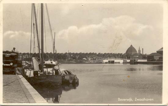 Zwaaihaven
Een mooie ansichtkaart van de haven, waarvan dit deel de zwaaihaven werd genoemd omdat het hier iets breder was en de schepen konden keren. De kaden aan deze zijde werden de Nieuwekade en de Zuiderkade genoemd. Rechts op de kaart zien wij de St. Agathakerk, de Ned.Herv.Kerk (Wijkertoren) en de schoorsteen van de Beverwijkse Conservenfabriek. De brug over de doorgang naar de binnenhaven (de Meer), als ook de Nieuweweg, lopend vanaf dit punt naar de spoorwegovergang in Velsen-N. In 1936 als een werklozenproject aangelegd en bij de aanleg van de Velsertunnel is dit geheel weer komen te vervallen.
Keywords: zwaaihaven de pijp bwijk