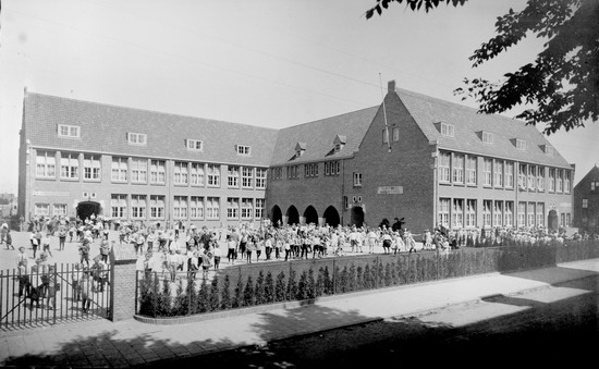 Heilighart school Beverwijk
Heilighart school Beverwijk. De foto van het 1e schooljaar met kinderen op het schoolplein: Het was niet gebruikelijk, cq het kwam niet voor (tot begin 70'er jaren) dat de jongens en meisjes gezamenlijk op het schoolplein speelden. Voor de foto echter, genomen door fotostudio Rembrandt uit Beverwijk, (foto Boumans), heeft de fotograaf gevraagd om ook de meisjes op het schoolplein te laten spelen. Volgens de heer Luc Beentjes van de Bankenlaan was er een streep over het schoolplein getrokken. De jongens moesten aan de linkerzijde blijven, de meisjes aan de rechterzijde. U kunt dit zien op de foto. Mijn moeder, Marie Leuring, staat ook op de foto. Zij staat rechts, het meisje met het jurkje met strik, rechts van de klimop. Deze foto is begin september 1930 genomen.

foto Cor Bart
Keywords: Heilighart school galgenweg