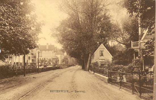 Zeestraat
Dit is het gedeelte van de Zeestraat richting Beeckzanglaan waarschijnlijk rond 1915. Het merkwaardige van dit deel van de Zeestraat is wel dat men aan de linkerzijde in Beverwijk woonde, maar de rechterzijde was de gemeente Wijk aan Zee en Duin. Op de foto zien wij de rails van de paardentram naar Wijk aan Zee welke tot 30 april 1924 dienst deed. Met die tram naar Wijk aan Zee was het eigenlijk raar gesteld, want van 1881 tot 1891 reed er een stoomtram welke de gasten op vlugge en comfortabele wijze moest vervoeren naar o.a. het Badhotel van Heinrich Tappenbeck. In 1891 verdween de stoomtram om plaats te maken voor een paardentram, immers de Badmaatschappij van Tappenbeck ging failliet en alle eigendommen werden overgenomen door de Buffetmaatschappij EPU en die maatschappij moest het financieel wat kalmer aan doen. De tram kon in 1924 de concurrentie met de autobus echter niet langer aan en verdween. 
Op de foto zien wij geheel rechts het houten huisje dat de naam America droeg. In 1920 werd het pandje onbewoonbaar verklaard en volgens oude gegevens stortte het in februari 1927 spontaan in en werd gesloopt. In een van de huizen aan de linkerzijde woonde Meester van Lingen, hoofd van de openbare lagere school aan de Breestraat waar later het Luxor-theater werd gevestigd, dat ondertussen ook al weer verdwenen is. Meester van Lingen was een vooraanstaand man in Beverwijk, bestuurslid van vele verenigingen, en op 1 maart 1932 werd de verbindingsstraat tussen de Koningstraat en de toenmalige Schoollaan (nu Prins Bernhardlaan), tot dat ogenblik officieel bekend als Dwarsstraat-Koningstraat, door de raad van de gemeente genoemd Meester van Lingenlaan, maar eigenlijk was dat slechts een bevestiging, want in de volksmond werd dat laantje reeds zo genoemd.
Keywords: zeestraat bwijk