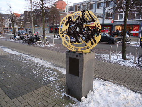 Monument voor tolvrijdom en stadskleur
Wat of wie is Beverwijk? Wat is het precies wat deze stad maakt tot de stad die zij nu is? De kunstenaars Jaap Velserboer en Willem Bakkum kregen de opdracht om een kunstwerk voor de Breestraat te maken. Zij speurden in het verleden naar de identiteit van onze stad. Terug naar de bron dus. Beverwijk begon haar bestaan in de middeleeuwen als een stadje waar druk en levendig werd gehandeld. Graaf Jan 1 van Holland en Zeeland  erkende de belangrijke positie van Beverwijk als handelknooppunt en verleende in 1298 stadsrechten. Het zegel ofwel de officiële handtekening van diezelfde graaf vormde het uitgangspunt voor dit kunstwerk. Wat u in de zegel ziet is een man te paard met een zwaard. De ruiter galoppeert bijna weg uit kunstwerk, het geldstuk dat de stadsrechten verbeeldt. Misschien komt dat wel door het ‘luxaflex’ effect, dat nog eens wordt versterkt door  de verschillende kleuren van het materiaal: donkerbruin staal en bladgoud. Op de hardstenen sokkel ziet men een bronzen plaquette met een ridderzegel van Graaf Jan 1 en de tekst: ‘Het past om de dingen die in de loop van de tijd voorvallen aan het geheugen van geschriften en aan de getuigenis van betrouwbare mannen toe te vertrouwen op dat ze niet met het verstrijken van de tijd verdwijnen’.
Het kunstwerk werd in 2002 geplaatst ter ere van de herinrichting van de Breestraat en werd bekostigd door plaatselijke aannemers. 

Bron: Blik op Beeld, Tekstbureau Zonneveld & Thöne i.o.v. gemeente Beverwijk, 2006.
Foto en bewerking: Co Backer
Keywords: bwijk Openbare Kunstwerken