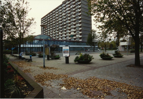 Wijkerbaan met zicht op het oude stadhuis
In 1965 werd het door ir. H.Nefkens gebouwde stadskantoor met woningen of zoals het officieel genoemd werd; “Een volledig stadhuis met, aanhangsel van een hoog woongebouw, bestaande uit premie-woningen en woningen in de sector” in gebruik genomen. Van monumentaliteit is bij dit gebouw nooit sprake geweest en dat er  ook niet gesproken kon worden van representatief gemeentehuis was toch wel te wijten aan het stelsel van de rijksgoedkeuringen op grond van art17. van de toenmalige wederopbouwwet. Een rijksgoedkeuring voor een gemeentehuis zou Beverwijk waarschijnlijk niet gekregen hebben, maar in een complex dat voor 60% van de inhoud uit woningen bestaat mag voor 40% een andere bestemming hebben. 

Maar hoe het ook zij ir. Nefkens heeft er het beste nee het allerbeste van gemaakt. Schaamtevol sprak men daarom in Beverwijk over het “stadskantoor”maar die wel alles bezat dat een stadhuis moest bieden: een raadszaal, een vergaderkamer van B&W, commissiekamers etc. Nefkens had een ondankbare taak , maar heeft zich er knap van gekweten. 
Het borstbeeld van J.F. Kennedy, aangeboden door de Algemene Bank Nederland,  werd op 6 januari 1965 gelijktijdig met de opening van het Stadskantoor onthuld. Dick Stins heeft dit beeld in brons uitgevoerd. Nu staat het in de opslag, maar zal worden teruggeplaatst als de nieuwbouw 0p de Wijkerbaan gereed is. Deze ansichtkaart werd op 27 augustus 1969 vanuit Beverwijk verstuurd naar de plaats Grouw in Friesland. 

Tekst: Co Backer
Keywords: bwijk Wijkerbaan